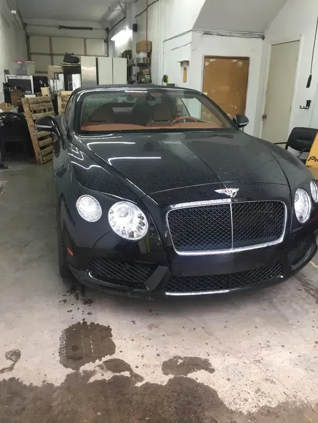 A black Bentley Continental GT coupe parked inside a garage with a tan leather interior visible.