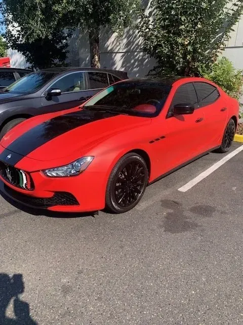 A bright red Maserati sedan with a thick black racing stripe down the center, parked in an outdoor lot.