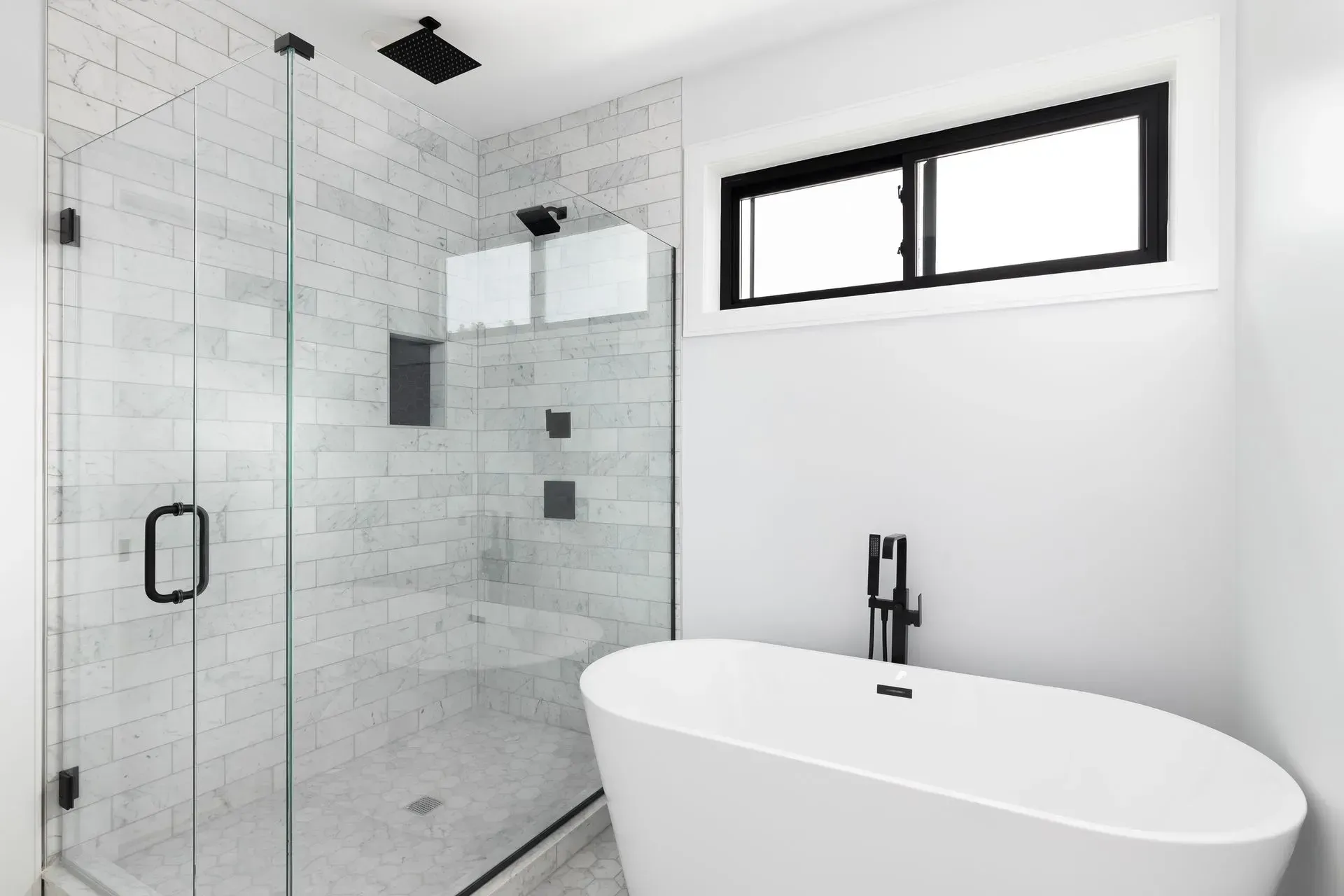 Modern bathroom featuring a glass-enclosed shower with white subway tiles and a freestanding white bathtub.