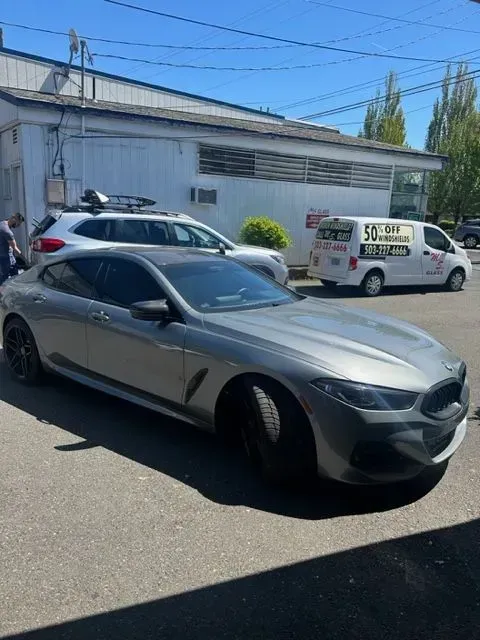 A silver BMW Gran Coupe parked in a lot in front of a white building, with a van and SUV visible in the background.