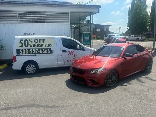 A red BMW parked next to a white van with 