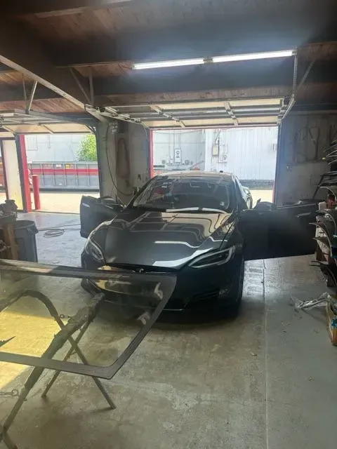 A dark grey Tesla parked inside a garage with its driver and passenger doors open.