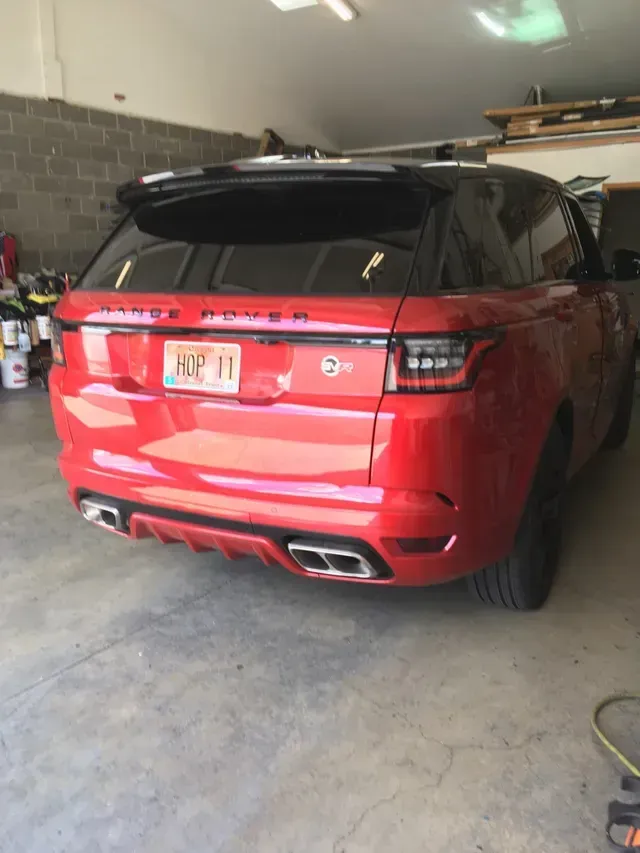 A red Range Rover parked in a garage, showcasing its rear exterior, spoiler, dual exhaust pipes, and license plate.