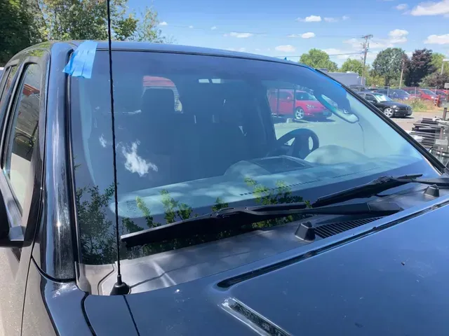 Close-up of a black truck's windshield with a piece of blue painter's tape on the upper corner and an external antenna.