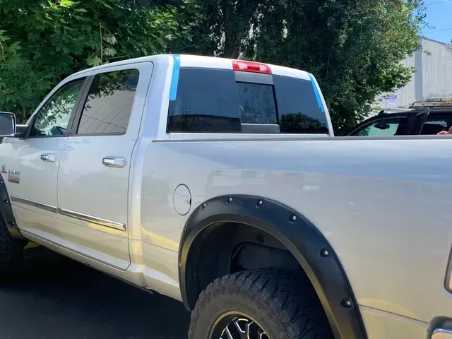 A silver pickup truck parked outdoors, featuring black fender flares with visible bolts and blue tape on the rear window.