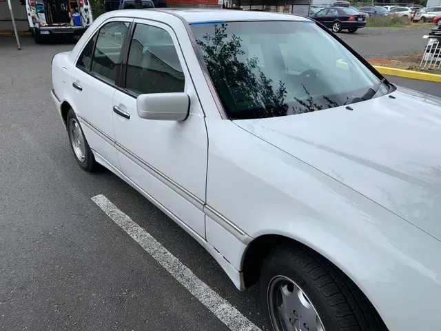 A white Mercedes-Benz sedan parked in an outdoor lot, viewed from the front passenger side.