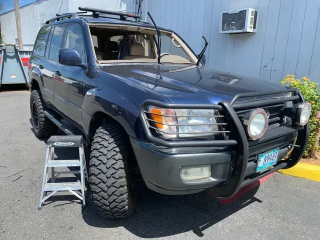 A dark blue Toyota Land Cruiser with off-road tires and a front grille guard parked near a building.