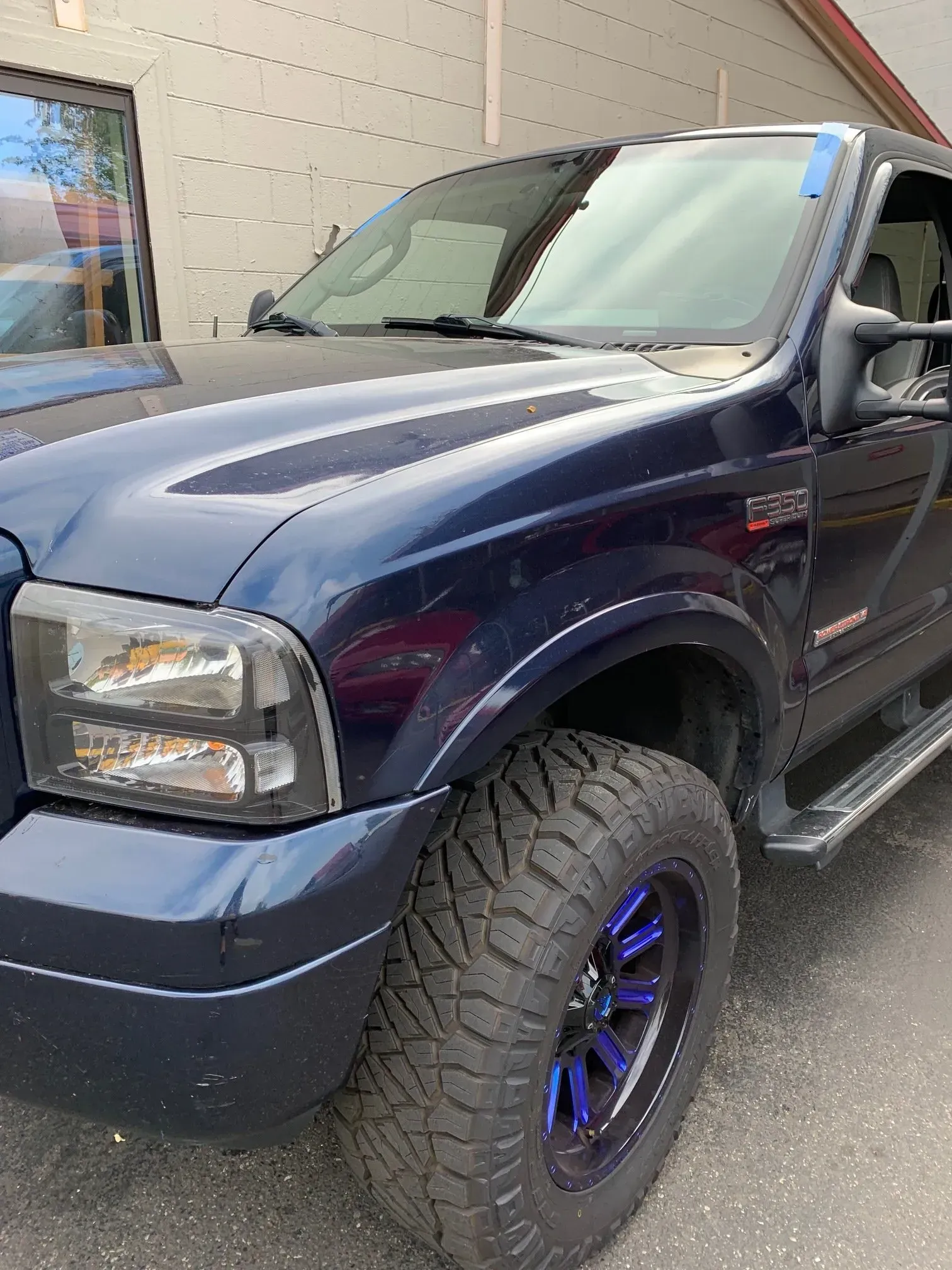 Blue Ford pickup truck with black headlights and blue-accented wheels parked near a building.