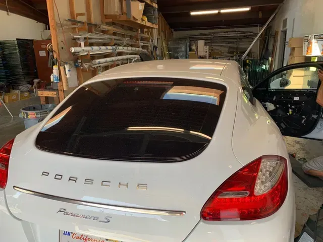 A white Porsche Panamera S in a garage, shown from the rear with the passenger door open.