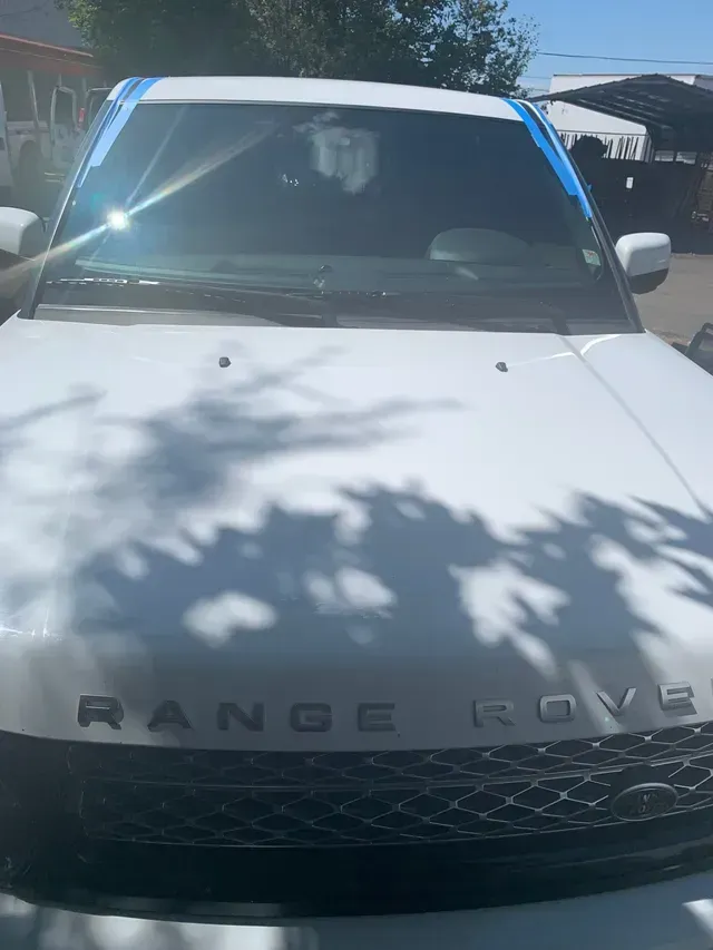Front view of a white Range Rover with blue painter's tape along the top edge of the windshield.