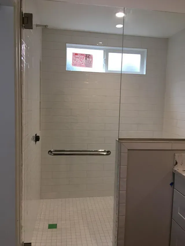A tiled walk-in shower with a silver horizontal grab bar mounted on the back wall and a rectangular window above.
