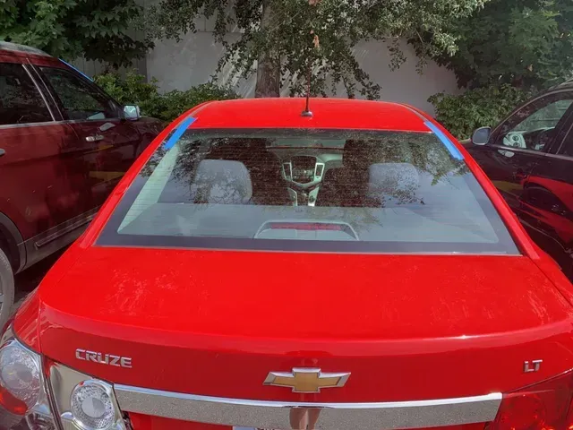 A red Chevrolet Cruze LT parked outdoors, viewed from behind with blue tape along the top edge of the rear windshield.