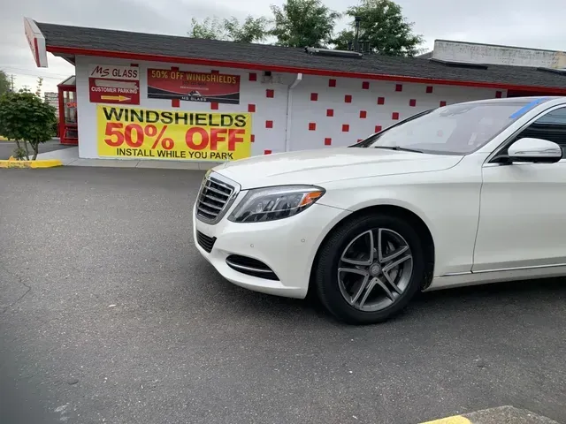 A white Mercedes sedan parked in front of an auto glass business advertising 50% off windshields.