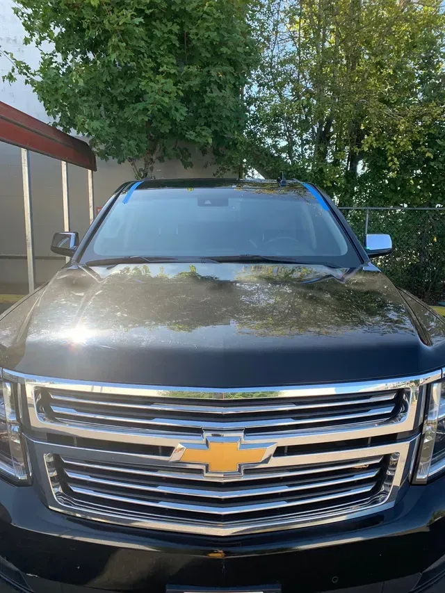 Front view of a dark-colored Chevrolet SUV parked outside with blue painter's tape on the windshield frame.