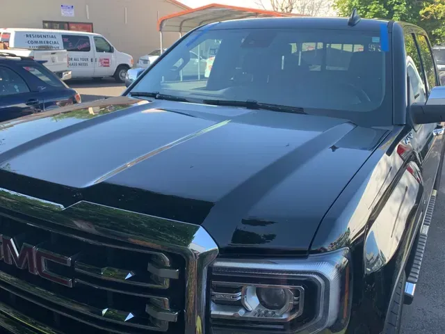 A front-angle view of a black GMC pickup truck parked in an outdoor lot on a sunny day.
