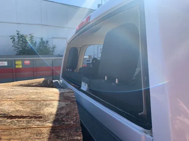 A close-up view through the rear window of a white truck, showing wooden planks loaded in the truck bed.