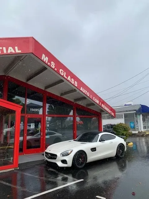 A white Mercedes-Benz sports car parked in front of a red storefront labeled 