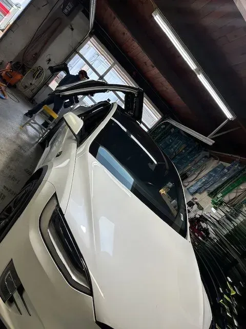 A white Tesla Model X with its falcon-wing door open inside a service or repair garage.