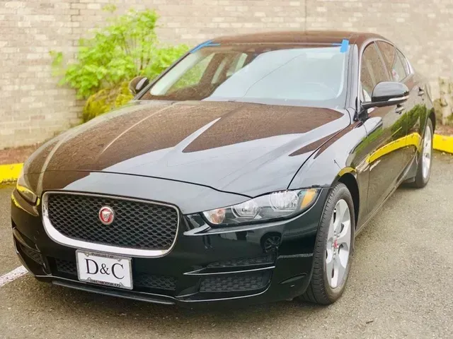 A black Jaguar sedan parked in an outdoor lot with a light-colored brick wall in the background.