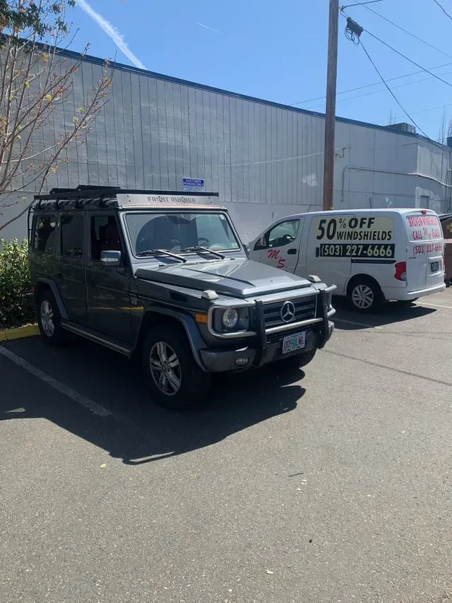 A grey Mercedes-Benz G-Class SUV parked in a lot next to a white van with 