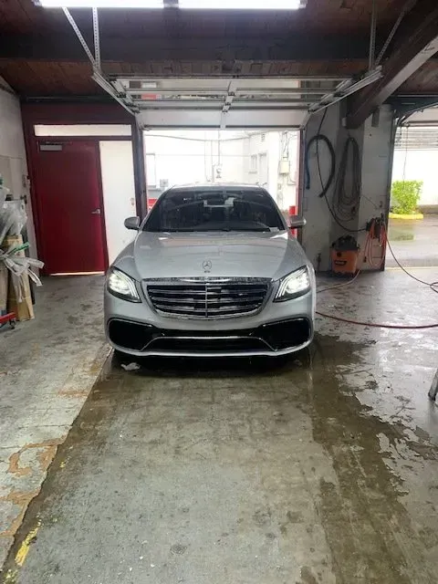 A silver Mercedes-Benz sedan parked inside a wet, industrial-style garage with the headlights on.