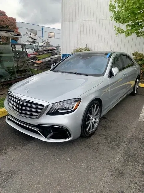 A silver Mercedes-Benz S-Class sedan parked on an asphalt lot next to a white industrial building.