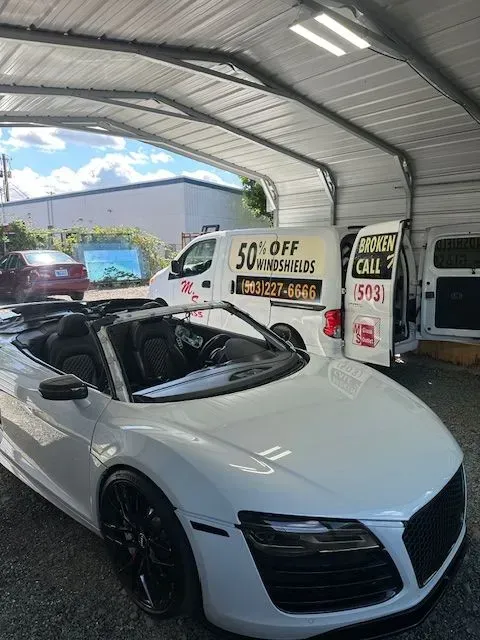 A white Audi convertible parked inside a garage next to a service van advertising windshield repair services.