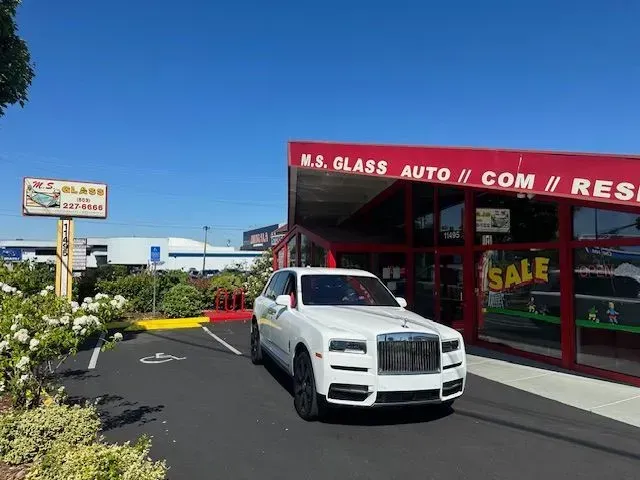 A white Rolls-Royce parked in front of an M.S. Glass store with a red awning under a clear blue sky.