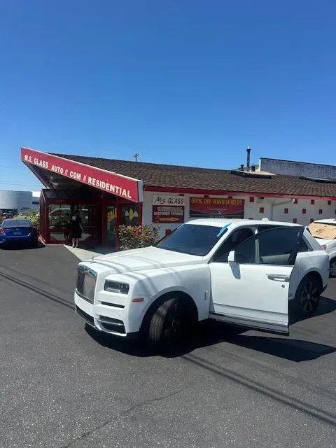 A white Rolls-Royce SUV parked in front of a building with a red sign, with the driver-side door open.