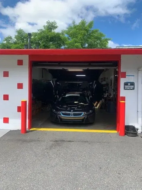 A black BMW i8 with doors open parked inside a garage featuring a white wall with red square accents.