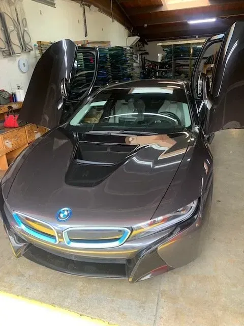 A gray BMW i8 with its iconic butterfly doors open, parked inside a spacious garage or workshop.