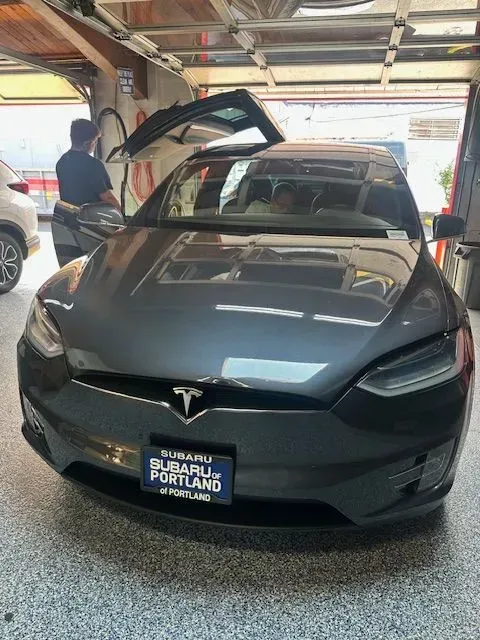 A grey Tesla Model X with its falcon-wing door open, parked inside a garage.