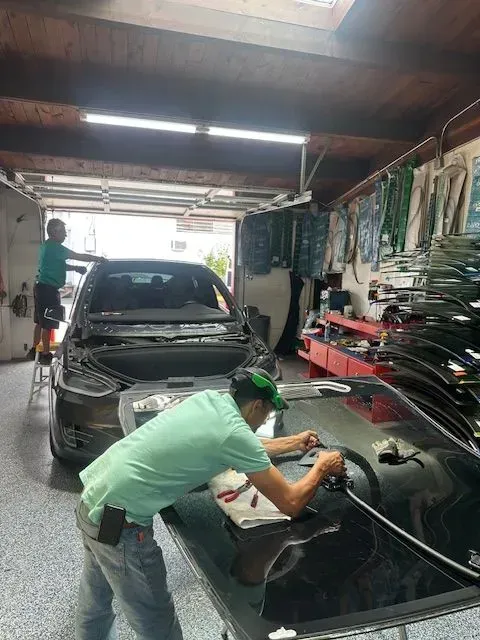 Two people working in a garage to install a new windshield onto a car.