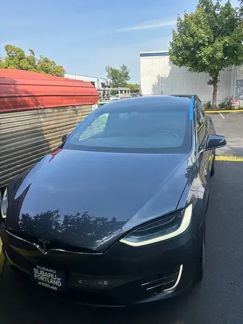 A dark gray Tesla Model S parked in a lot, with a Subaru of Portland dealership plate visible on the front bumper.