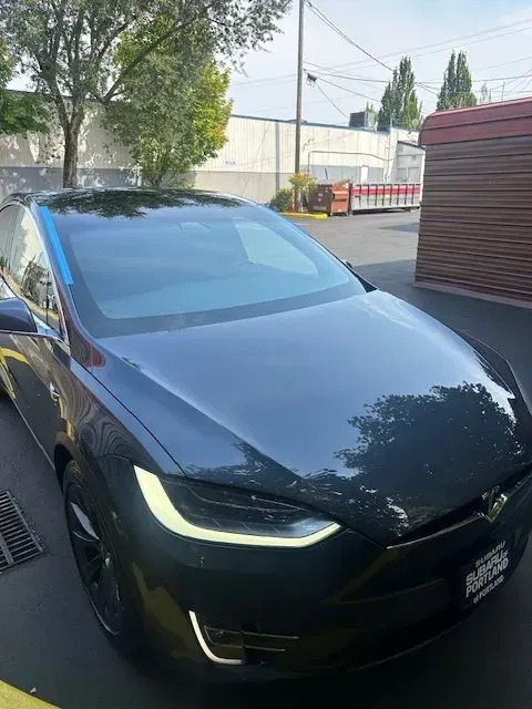 A dark gray Tesla Model S parked on asphalt in an outdoor lot on a sunny day.