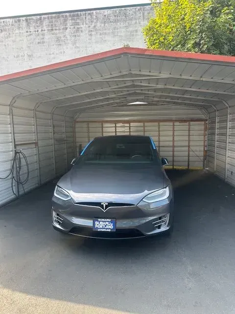 A grey Tesla Model S parked inside a metal carport.