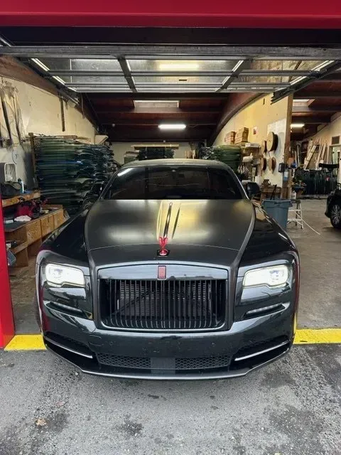 Front view of a matte black Rolls-Royce parked inside a spacious garage with a red frame and concrete floor.
