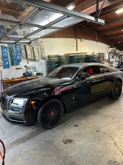 A black Rolls-Royce Wraith with custom red-accented wheels and red interior parked inside a cluttered industrial garage.