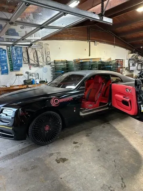 A black Rolls-Royce Wraith with custom red interior and wheels parked inside a garage with its driver-side door open.