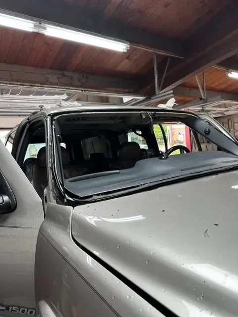 A silver pickup truck parked in a garage with its windshield removed, revealing the interior dashboard and roof frame.