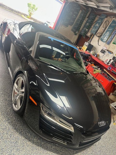 Black sports car in a garage, front view with glossy finish and aftermarket wheels