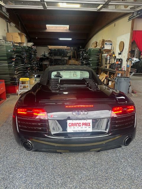 Dark red convertible sports car parked inside a cluttered auto shop garage
