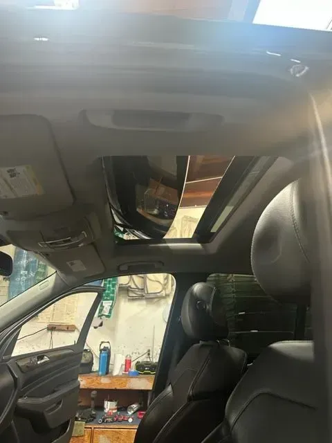 Interior of a car showing black leather seats and an open sunroof against a bright, hazy sky.