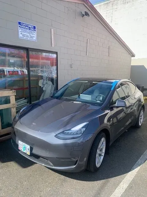 A gray Tesla parked in front of a tan concrete building with glass windows.