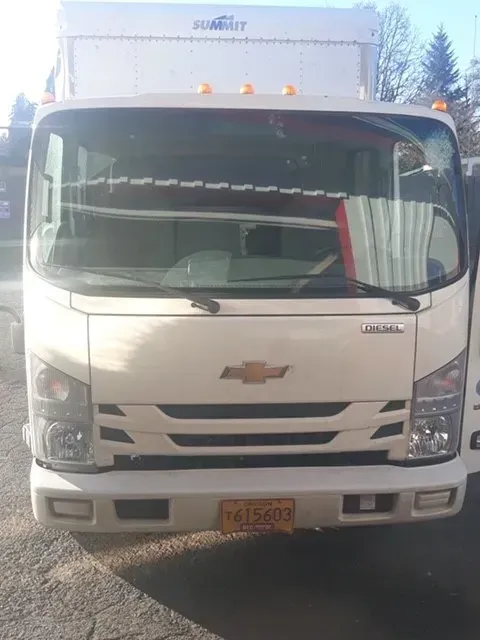 Front view of a white Chevrolet cab-over box truck parked outdoors under a bright sky.