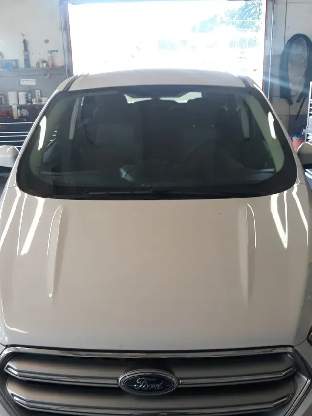 Front view of a white Ford vehicle hood and windshield in an automotive garage.