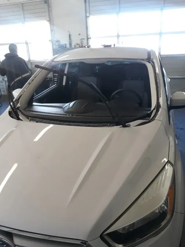 White vehicle inside a garage with its windshield removed, showing the frame and wipers exposed.