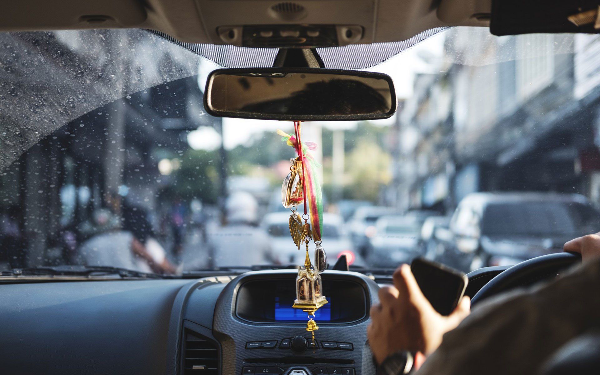Interior car view, driver holding phone, looking at a busy street.
