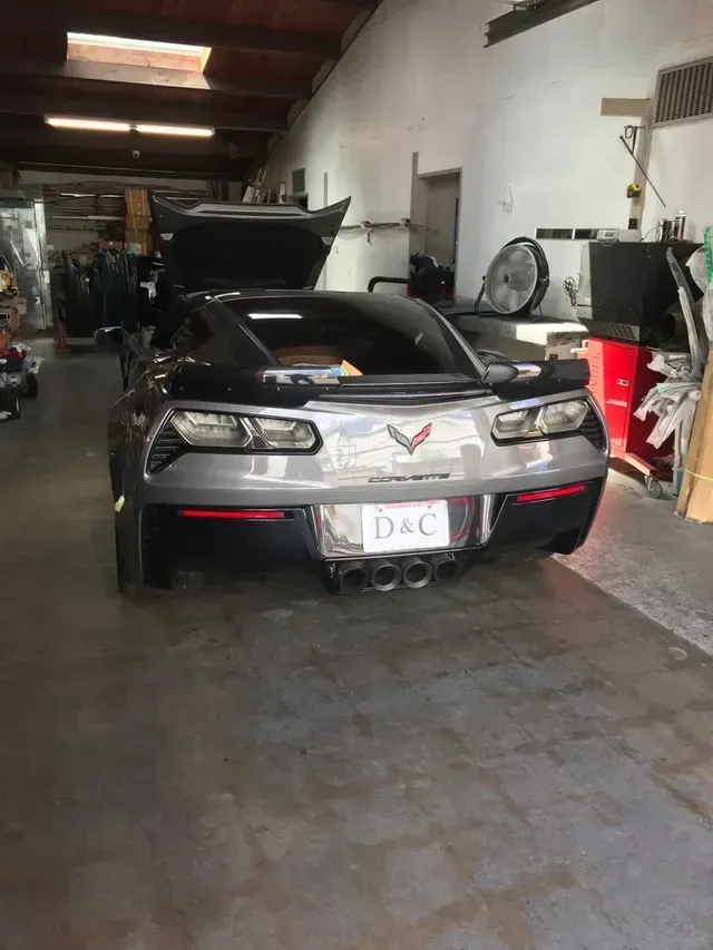 A silver Chevrolet Corvette parked inside a workshop with its trunk open.