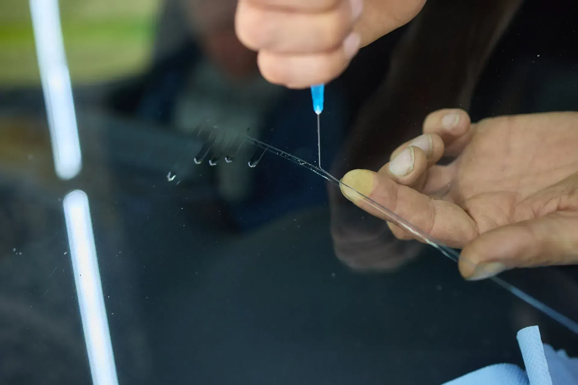 A person using a thin needle to inject resin into a crack in a car windshield.